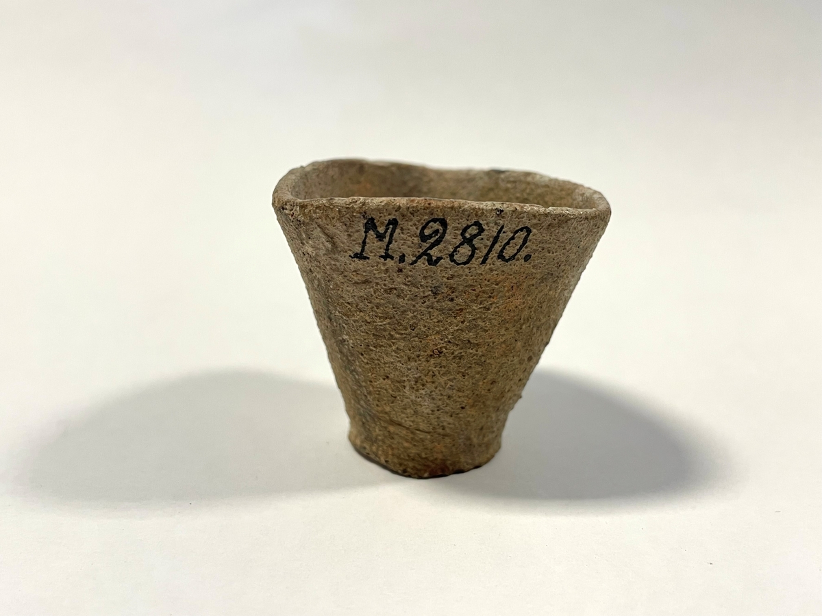 Trekantigt formad degel i tunt, ljusbeigt, sandmagrat lergods. Cirkulär botten. Benämns "Hessisk degel" i Smålands museums huvudkatalog. Möjligen för smältning av metaller.