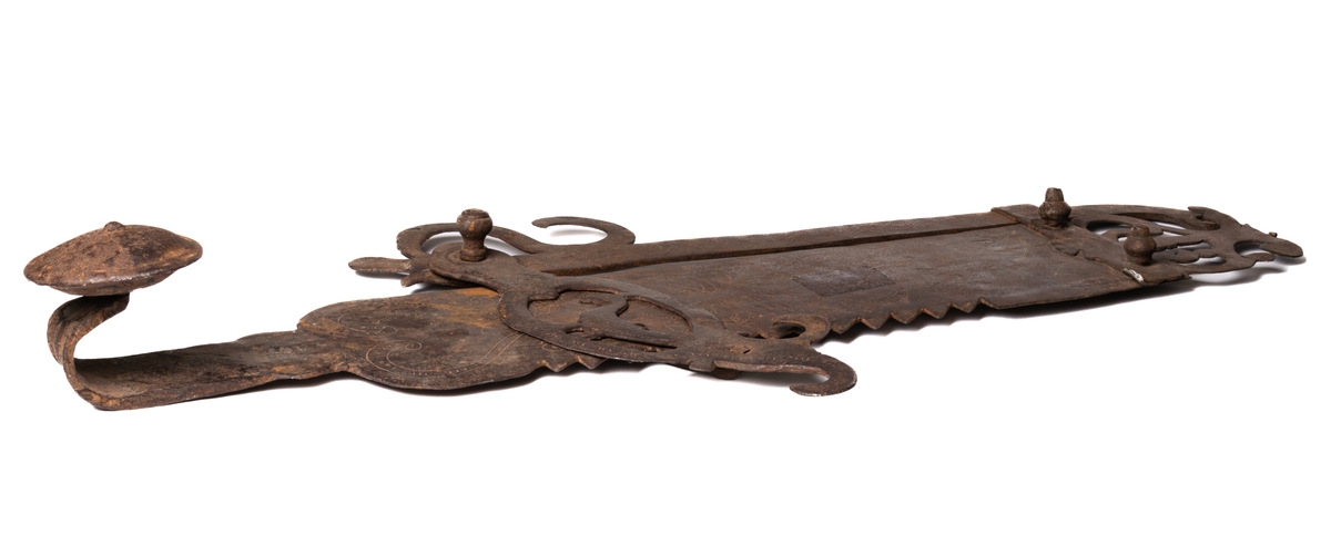 Järnföremål, okänd användning. Möjligen slangringsregel till stor ugn. Märkt 1799.
Avlångt med brutna ornament vid ändanrna liknande krona och fågelfigur.
Till vänster ett kraftigt knoppformigt handtag. Framsidan täckt av ristade ornament: slingor med glesa tvärstreck, blommor, m.m.
Otydligt smedsmärke, se skiss.