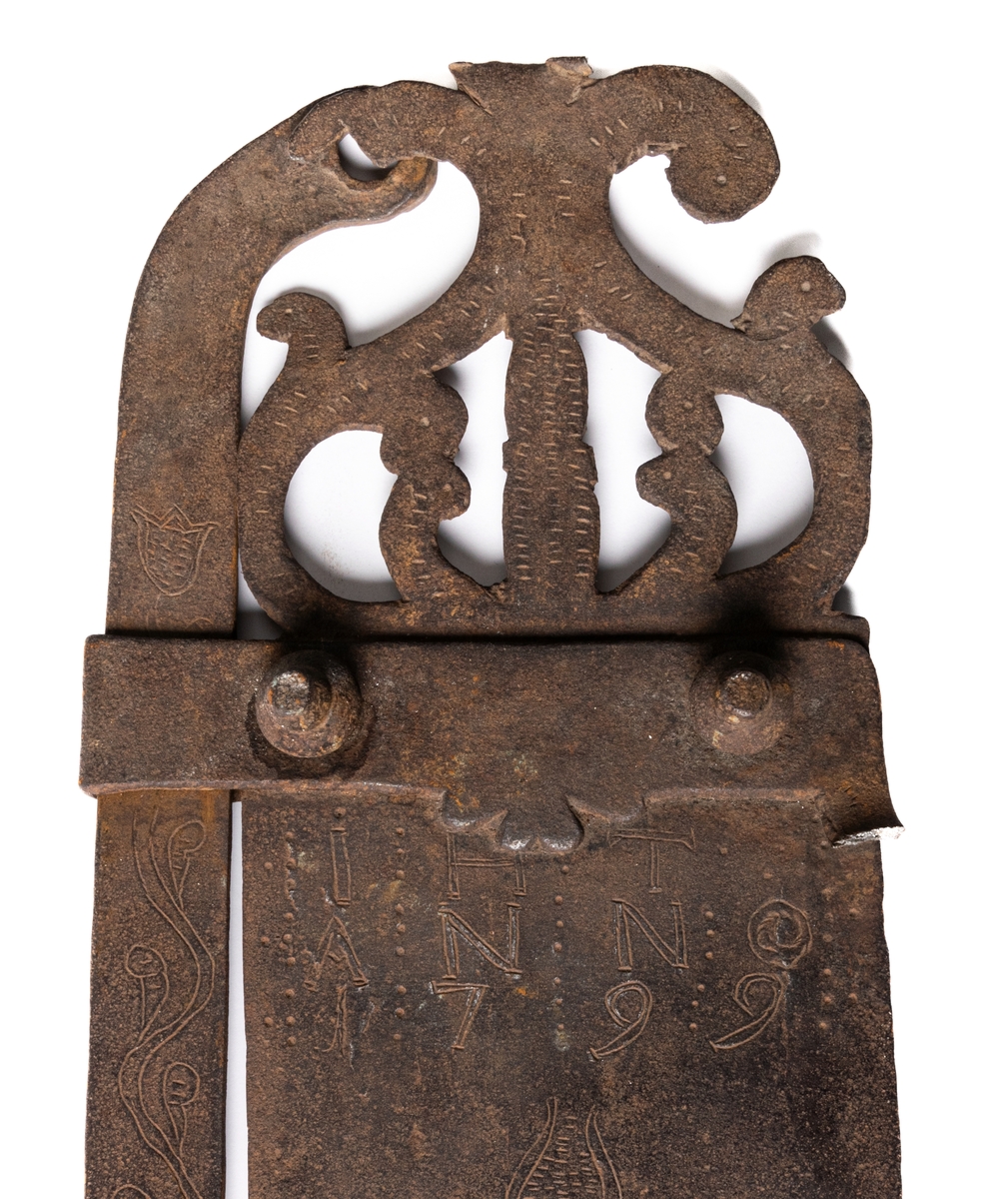 Järnföremål, okänd användning. Möjligen slangringsregel till stor ugn. Märkt 1799.
Avlångt med brutna ornament vid ändanrna liknande krona och fågelfigur.
Till vänster ett kraftigt knoppformigt handtag. Framsidan täckt av ristade ornament: slingor med glesa tvärstreck, blommor, m.m.
Otydligt smedsmärke, se skiss.