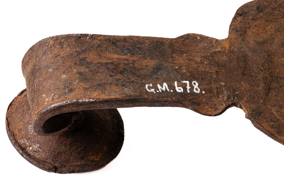 Järnföremål, okänd användning. Möjligen slangringsregel till stor ugn. Märkt 1799.
Avlångt med brutna ornament vid ändanrna liknande krona och fågelfigur.
Till vänster ett kraftigt knoppformigt handtag. Framsidan täckt av ristade ornament: slingor med glesa tvärstreck, blommor, m.m.
Otydligt smedsmärke, se skiss.
