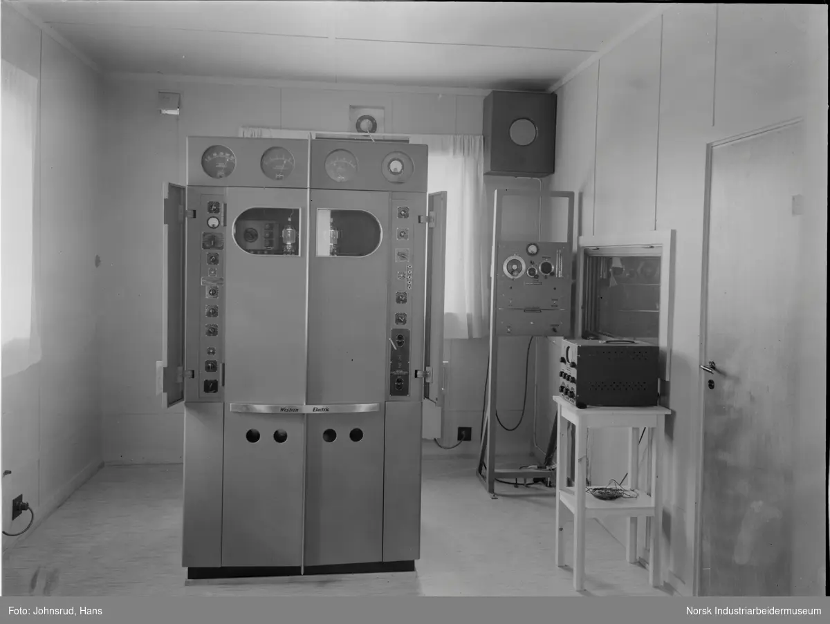Interiør relestasjon for Notodden Kringkaster. Western Electric maskin stående midt i rommet.