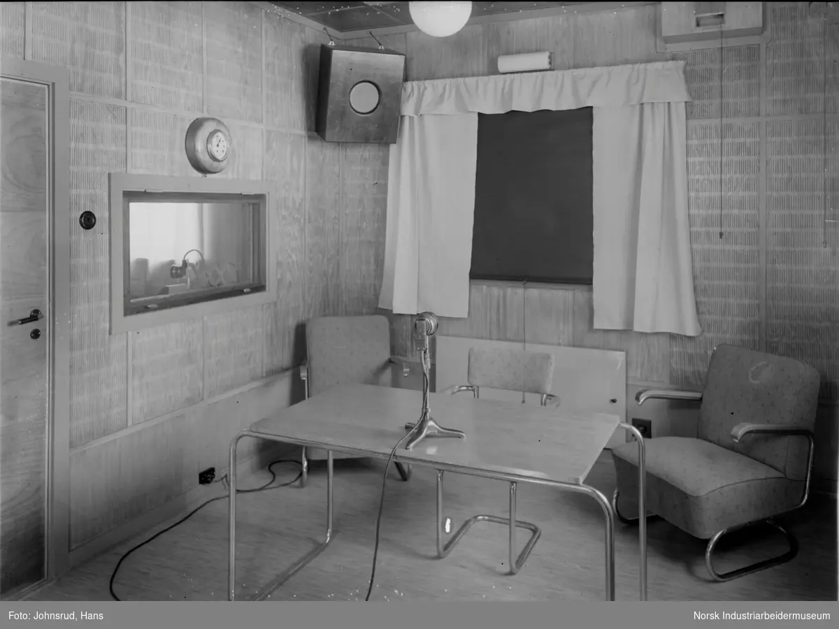 Interiør relestasjon for Notodden Kringkaster. Studio med stoler og mikrofon midt på bordet.