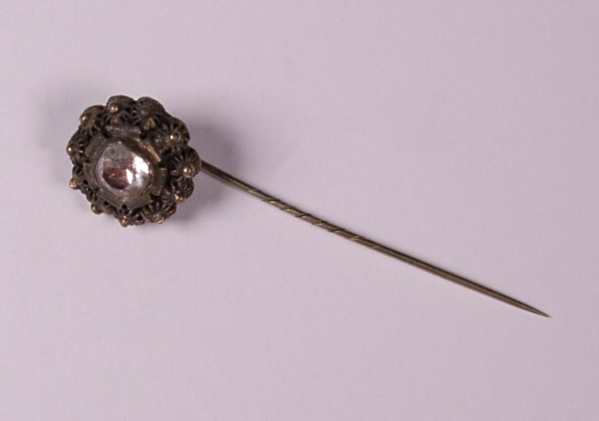 Kvadratisk facettslipad sten,(glas) infattad med en krans av små metallblommor.
Av silver, L 58 mm