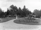 Fotografi ur Linköpingsfotografen Didrik von Essens samling som länge hänförts till Linköpings trädgårdsförening. Nya observationer placerar istället motivet till trädgården till familjen Blüms hem på Barnhemsgatan 4. Till vänster står närmare bestämt Gösta Blüm intill en oidentifierad kvinna. I mitten ser vi Hildur Setterberg och Adolf Blüm. Till höger står Amanda Lorentzon och Ellen Blüm. Bilden har lämnats oss odaterad men Adolf Blüms död 1901 skänker viss ledning.