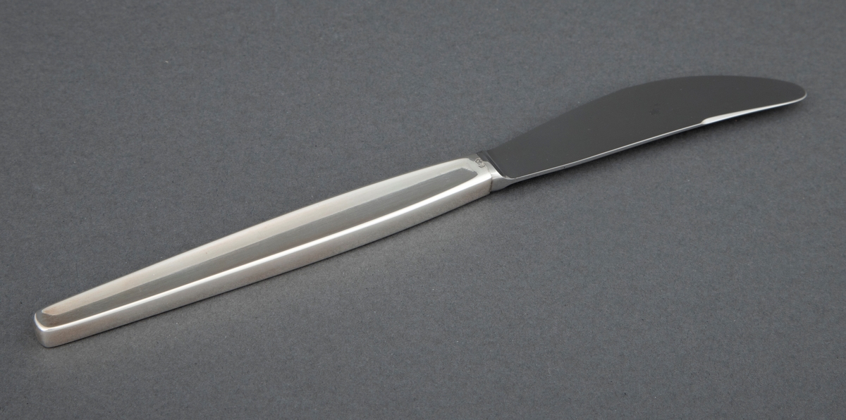 Kniv i sølv. Skaftet har rektangulært snitt, og i hele skaftlengden en ergonomisk og dekorativ forsenkning i midten på to sider. Bladet er i stål. og har buet egg.