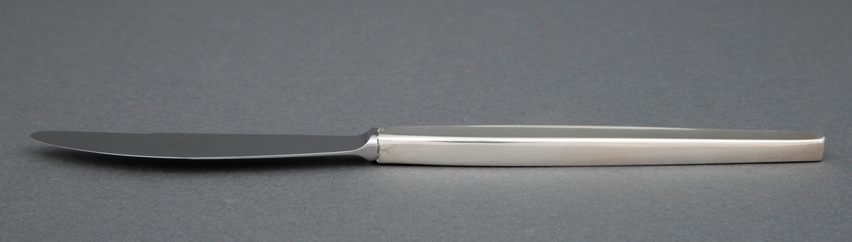 Kniv i sølv. Skaftet har rektangulært snitt, og i hele skaftlengden en ergonomisk og dekorativ forsenkning i midten på to sider. Bladet er i stål. og har buet egg.