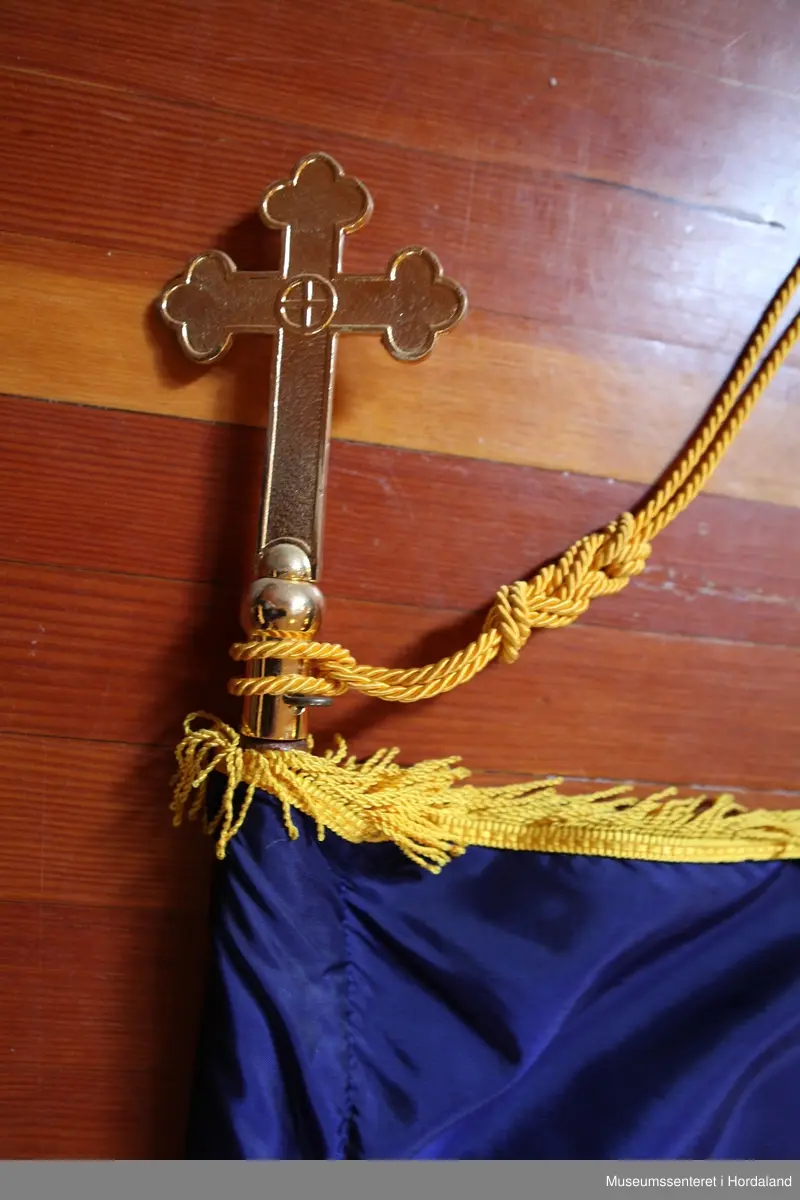 Rektangulært, hvitt flagg med et firkantet blått felt i øvre venstre hjørne med et rødt kors. Rundt flagget er en gul frynsekant. Flagget er festet til en paradestang av tre med et gyllent kors på toppen. Under dette korset er en gul snor knytt sammen ved stangen, den deler seg og ender i to dusker. Selve stangen ender i et messingledd som kan festes til en forlengelse av stangen.