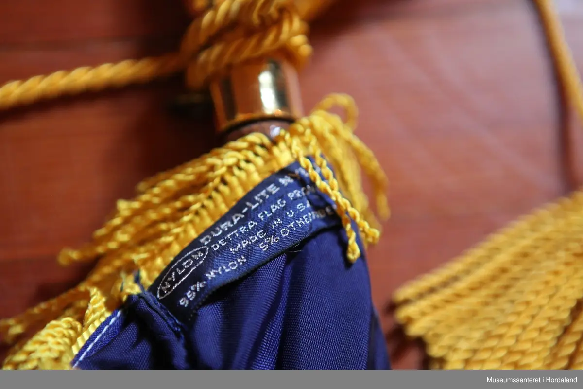 Flagg med stang i to deler. Flagget er rektangulært, hvitt med et firkantet blått felt i øvre venstre hjørne med et rødt kors. Rundt flagget er en gul frynsekant. Flagget er festet til en paradestang av tre med et gyllent kors på toppen. Under dette korset er en gul snor knytt sammen ved stangen, den deler seg og ender i to dusker. Selve stangen kan tas fra hverandre i et messingledd i midten.