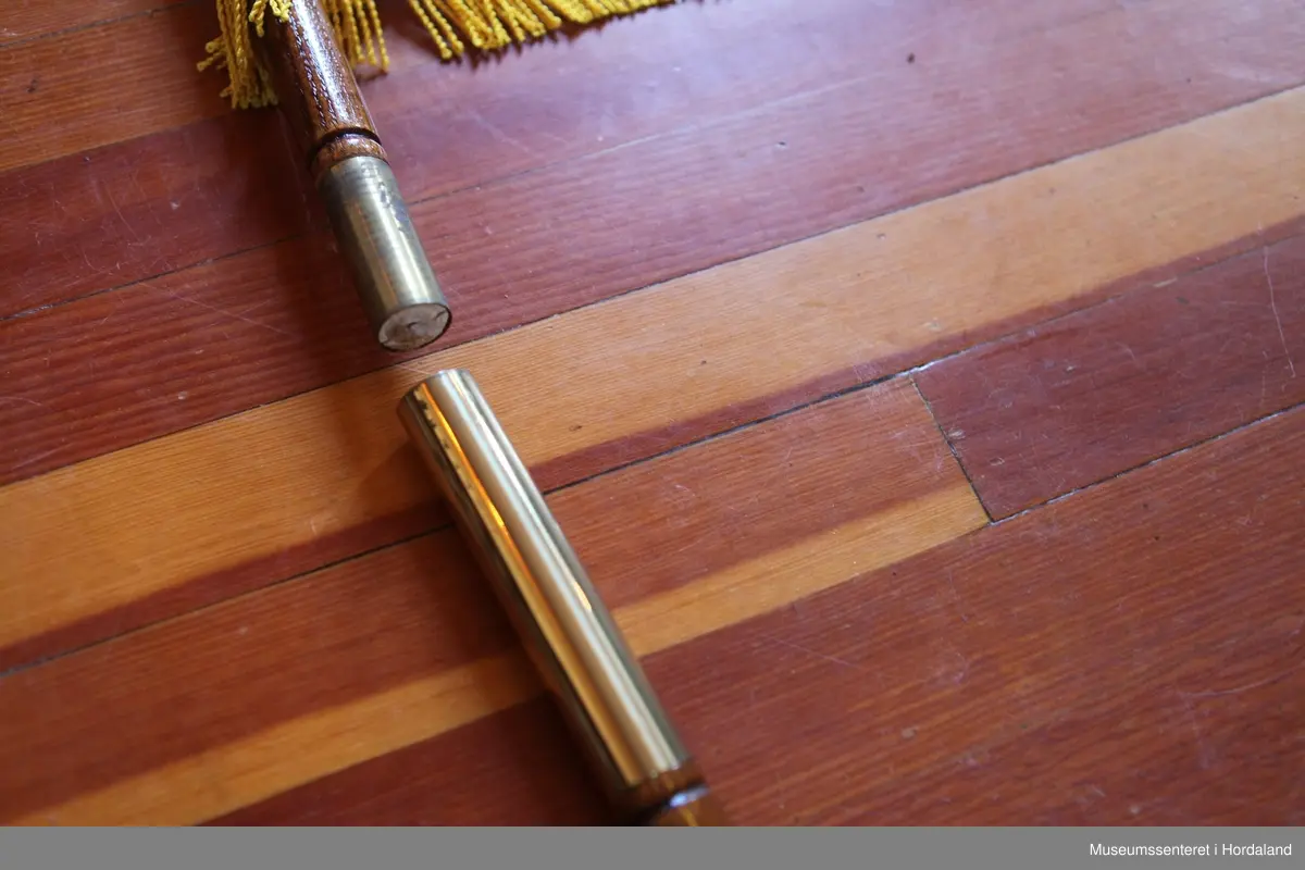 Flagg med stang i to deler. Flagget er rektangulært, hvitt med et firkantet blått felt i øvre venstre hjørne med et rødt kors. Rundt flagget er en gul frynsekant. Flagget er festet til en paradestang av tre med et gyllent kors på toppen. Under dette korset er en gul snor knytt sammen ved stangen, den deler seg og ender i to dusker. Selve stangen kan tas fra hverandre i et messingledd i midten.