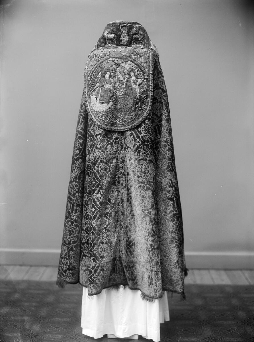 Korkåpa av skuren brungul sammet (ursprungligen röd) med granatäpplemönster och broderier. Kåpan är daterad till Sturegotiken och är troligen ett Vadstena-arbete.

Längs kåpans ytterkant ett band i rött, blått och guld, kantat av silkesfrans randad i flera partier i ursprungligen rött och grönt - nu gulgrått. Utmed framkanterna linnebårder med figurer i aediculor, guld, silver och mångfärgat silke. Å högra sidan jungfru Maria, Petrus, Johannes Döparen, helgon med stav och helgon med kors. Å vänstra sidan okända helgon, Sankt Paulus, Sankt Andreas och okänd apostel med spjut. Figurerna inom rundbågar av guld, på marken strödda blommor.

Vid nacken på rött ylle (ursprungligen täckt av rött taftliknande siden) syns Kristus som smärtoman i halvfigur omgiven av två Guds lamm, på dipens Marie bebådelse med inskrift "AVE MARIA GRA". På broderierna strödda metallpajletter.

Tyget är troligen vävt i Italien under 1400-talets andra hälft. Kåpans montering med band och silverfrans är ursprunglig och kan dateras till 1400-talets senare del eller omkring 1500. Broderierna är troligen utförda i Tyskland under 1400-talets andra hälft. Brämets broderi delvis ibroderat, troligen under 1600- eller 1700-talen.