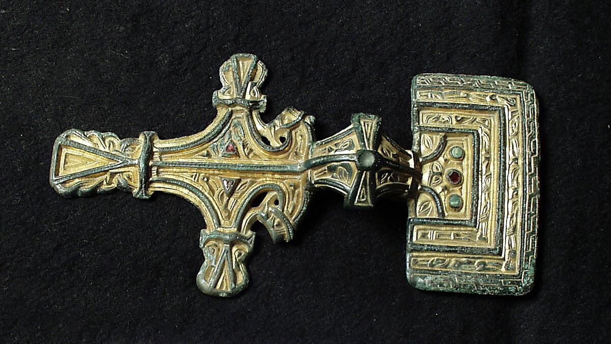 Förgyllt reliefspänne av brons. Rektangulär huvudplatta (63 x 36 mm) och rombisk fot med utskott på var sida. Ornamentik i relief samt iläggningar av tre granater och två gröna stenar. På baksidan nålhållare och nål. Kompl nov 2006/ML
Av vit brons med sp.torn, 5 1/2 tum lång.  Åtskilliga fornfynd/ huvudnr: 1763 - 1807 /,  funna i backen vid Högbro i Roma i flera forngravar, under järnvägsarbetet där hösten 1877. Kanske har dessa vapen /av järn och stål/ använts i slaget år 1288 mellanWisbyborna och bönderna /anförda av Peder Hardings i Vall/ ; märkligt är dock att ett par aln djupare i backen hittades doningar av brons som visserligen är mycket äldre.  Se .V. Sägner, 116, III. 977. Strelow, S 144 och 5.