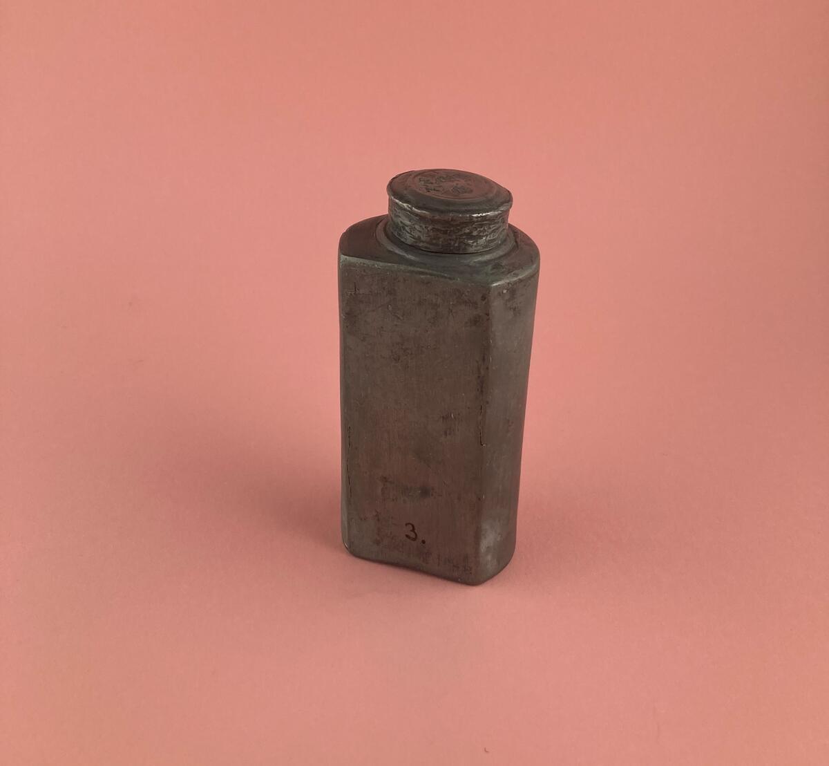 Vinflaska av tenn med fodral av läder. Vinflaskan är trekvartscylindrisk med en rak sida med skruvlock. Tillverkad i Melchior Lefflers verkstad. Stämplar på locket "N2" (@1795) samt två otydliga stämplar "H ? L" eller "M L" (Melchior Leffler). Att det är tvåstämplat är enligt "Tenngjutare i Sverige" mycket ovanligt.

Cylindriskt fodral av mörkt läder, öppnat i två halvor. Hål efter söm längs kanten. Stängningsanordning med hyska och hake, enkel ledad bärhank av järn, två gångjärn av järn, mkt stelt. "Möjligen det fodral som Ahrent Benicke gjorde till sockenbudskalken 1709 (räk.)" enligt "Sveriges kyrkor Gotland" Visby Domkyrka inredning sid 54.

Inköpt från Visby domkyrka (av donator?) enligt orginalkatalogen.
