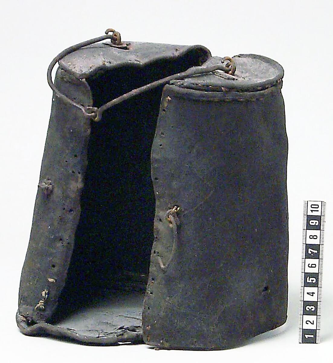 Vinflaska av tenn med fodral av läder. Vinflaskan är trekvartscylindrisk med en rak sida med skruvlock. Tillverkad i Melchior Lefflers verkstad. Stämplar på locket "N2" (@1795) samt två otydliga stämplar "H ? L" eller "M L" (Melchior Leffler). Att det är tvåstämplat är enligt "Tenngjutare i Sverige" mycket ovanligt.

Cylindriskt fodral av mörkt läder, öppnat i två halvor. Hål efter söm längs kanten. Stängningsanordning med hyska och hake, enkel ledad bärhank av järn, två gångjärn av järn, mkt stelt. "Möjligen det fodral som Ahrent Benicke gjorde till sockenbudskalken 1709 (räk.)" enligt "Sveriges kyrkor Gotland" Visby Domkyrka inredning sid 54.

Inköpt från Visby domkyrka (av donator?) enligt orginalkatalogen.