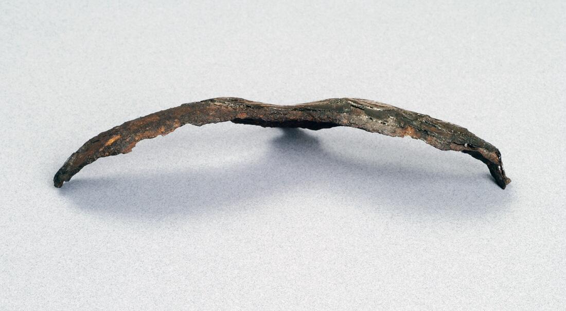 Detalj av hjälm. Av järn  närmast triskelformat skydd för ögonbryn  och näsa. Dekor av drakslingor i silver    kompl okt 1006/ml
i form av ögonbryn, av järn med drakslingor i silver. Funnen i lokrume.