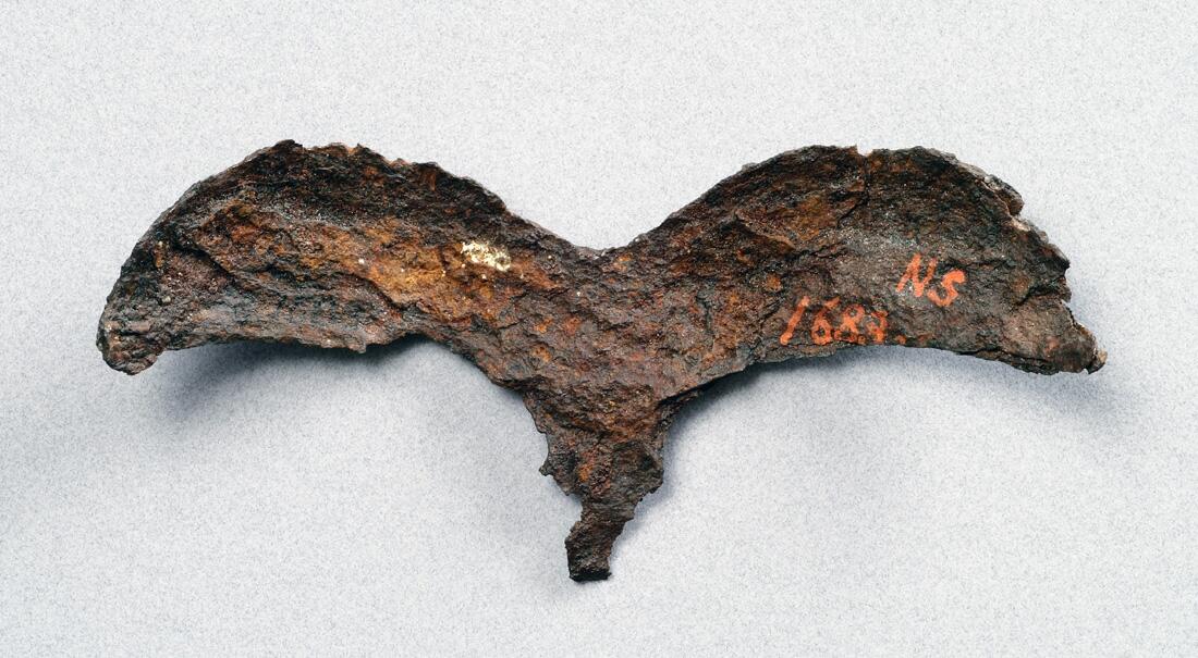 Detalj av hjälm. Av järn  närmast triskelformat skydd för ögonbryn  och näsa. Dekor av drakslingor i silver    kompl okt 1006/ml
i form av ögonbryn, av järn med drakslingor i silver. Funnen i lokrume.