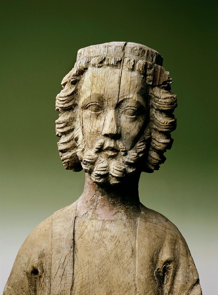 Skulptur av trä som föreställer tronande manligt helgon, troligen S:t Olof.

Han bär lång klädnad med mantel draperad över axlarna, överarmarna och knäna. Båda underarmarna saknas. Han har halvlångt, lockigt hår och skägg och på hjässan har troligen suttit en krona. Med sina skoklädda fötter trampar helgonet på en figur som ligger på mage. Denna figur bär slät hjälm och ansiktet uttrycker skräck. Dess ben och armar är skadade.

I ansiktet finns vissa färgrester kvar. Tronen är skadad och skulpturens baksida är urtagen.

Enligt Johnny Roosval i "Medeltida konst i Gotlands Fornsal" är skulpturen av ek och tillverkad av "Hamramästaren" och "Bungemästaren". Roosval daterar den till höggotik, cirka 1295-1330.

Enligt originalkatalogen är den på mage liggande figuren en romersk krigare - såsom kyrkan förtrampande den världsliga makten.