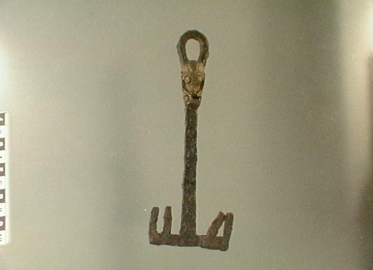 Huvudet består av en ögla nedanför denna pålagd bronsornamentik i form av växtornamentik stammen massiv med rektangulärt tvärsnitt dubbelsidigt ax enligt orginalkatalogen funnen under plöjning på ca 25 cm djup omkring 300 m från boningshuset
av järn, med bronsbeslag. Längd 167,5 mm. Från boticke i anga. Funnen under plöjning på 2,5 dm. Djup, omkring 300 meter från boningshuset. Enligt uppgift av a. Jansson.