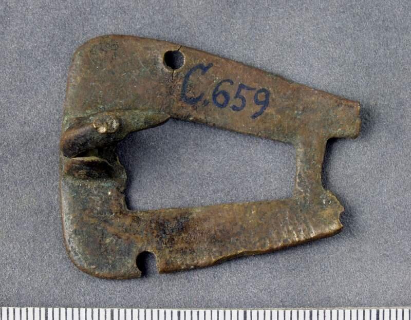 Del av botten till djurhuvudformigt spänne, nålfäste med en mycket kort bit av nålen bevarat, bottnens smalaste parti saknas,
djurhuvudformad, fragment av botten. 36 mm.