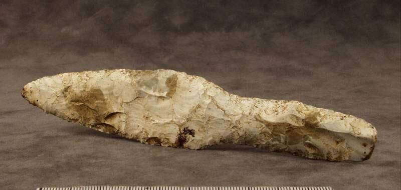 Av gråvit flinta  plant blad med finhuggna kanter handtaget har spetsovalt tvärsnitt  enligt orginalkatalogen funnen i klinteåker
l. 179 mm. Största br. 32 mm. Från klinte i follingbo. Funnen i klinteåker.