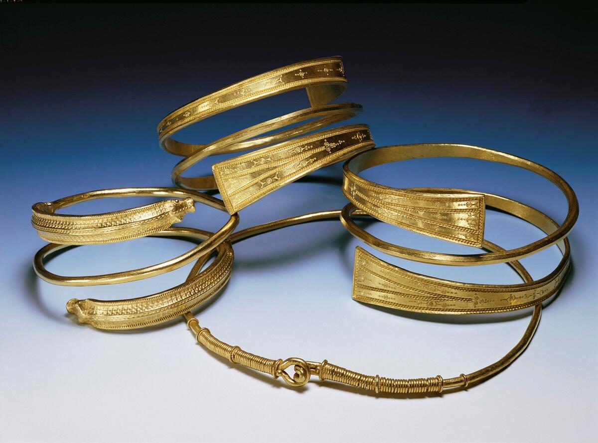 AV GULD, MED UTPLATTADE ÄNDAR, FÖRSEDD MED RIK STÄMPELORNAMENTIK. DIAM. 9,9 CM. FRÅN BURS 1'15, KÄLLUNGE. FUNNEN VID GRUSNING AV VÄG, DEN 9/6, 1954. GÄLLER FÖR HNR: 9991:1 - 4. VIKT 74 OCH 53 GRAM.