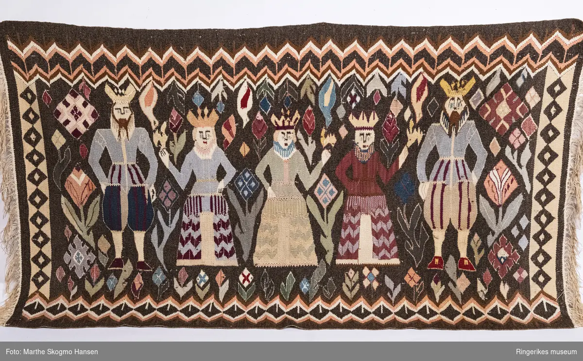 Veggteppe fra Tanberg. Teppet er vevd i gobelinteknikk, og med renningen på tvers og innslaget på langs. Motivet har mange farger, og flere sjatteringer av flere av fargene (for eksempel rosa, rød, gul og grønn). Motivet består av konger og dronninger. Det er to konger, en på hver side, og tre dronninger i midten. Alle har kroner på hodet. Kongene har skjegg, tunikaer og knebukser. Dronningene har lange kjoler, og er lavere enn kongene. Rund figurene er det stiliserte blomster og geometriske figurer. Mellom figurene er det fire fugler som ser ut som om de stuper nedover. På sidene og nedenfor figurene er det border med diamant-former av forskjellige typer. Over hovedmotivet går det en sikk-sakkbord. Bakgrunnen er mørkebrun. Teppet har frynser på hver side. Teppet er relativt lite slitt.