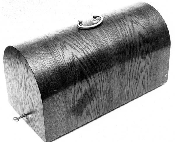 a) Symaskin av märket Husqvarna, modell V.S.4. Handdriven. Svartmålad på träplatta. Nersänkt låda med tillbehör. b) Huv av ekfaner. Handtag på toppen. c) Skyttel av stål. Rund, spetsig i ena änden, rak i den andra. Innehåller en spole med vit tråd. d) Fem spolar av stål. Rund stav med plattor i ändarna. Olika trådrester. e) Ledpressarfot (monterad på maskinen). f) Fållvikare 2 mm. g) Fållvikare 6 mm. h) Gansapparat. i) Rynkfot .j) Linjal. Längd 5,3 cm. k) Fem symaskinsnålar i olika grovlekar. Cellofanförpackning. l) Skruvnyckel. Typ lång platt nål, bakre delen försedd med runt hål. m) Skruvmejsel av stål. Fäste av svart bakelit. n) Borste av dubbelvriden ståltråd med en borste i ena änden. o) Skruvmejsel av stål. Fäste av svart bakelit. p) Provlapp av bomullsflanell. För kontroll av stygnställning. q) Provlapp av bomyllskypert. Till kontroll av stygnställning. r) Bruksanvisning. Tryckt broschyr på 30 sidor.