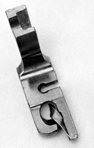 a) Symaskin av märket Husqvarna, modell V.S.4. Handdriven. Svartmålad på träplatta. Nersänkt låda med tillbehör. b) Huv av ekfaner. Handtag på toppen. c) Skyttel av stål. Rund, spetsig i ena änden, rak i den andra. Innehåller en spole med vit tråd. d) Fem spolar av stål. Rund stav med plattor i ändarna. Olika trådrester. e) Ledpressarfot (monterad på maskinen). f) Fållvikare 2 mm. g) Fållvikare 6 mm. h) Gansapparat. i) Rynkfot .j) Linjal. Längd 5,3 cm. k) Fem symaskinsnålar i olika grovlekar. Cellofanförpackning. l) Skruvnyckel. Typ lång platt nål, bakre delen försedd med runt hål. m) Skruvmejsel av stål. Fäste av svart bakelit. n) Borste av dubbelvriden ståltråd med en borste i ena änden. o) Skruvmejsel av stål. Fäste av svart bakelit. p) Provlapp av bomullsflanell. För kontroll av stygnställning. q) Provlapp av bomyllskypert. Till kontroll av stygnställning. r) Bruksanvisning. Tryckt broschyr på 30 sidor.