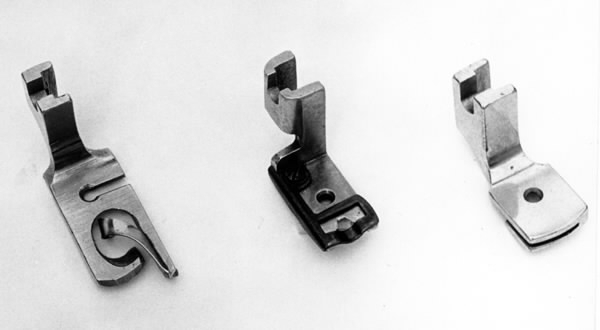 a) Symaskin av märket Husqvarna, modell V.S.4. Handdriven. Svartmålad på träplatta. Nersänkt låda med tillbehör. b) Huv av ekfaner. Handtag på toppen. c) Skyttel av stål. Rund, spetsig i ena änden, rak i den andra. Innehåller en spole med vit tråd. d) Fem spolar av stål. Rund stav med plattor i ändarna. Olika trådrester. e) Ledpressarfot (monterad på maskinen). f) Fållvikare 2 mm. g) Fållvikare 6 mm. h) Gansapparat. i) Rynkfot .j) Linjal. Längd 5,3 cm. k) Fem symaskinsnålar i olika grovlekar. Cellofanförpackning. l) Skruvnyckel. Typ lång platt nål, bakre delen försedd med runt hål. m) Skruvmejsel av stål. Fäste av svart bakelit. n) Borste av dubbelvriden ståltråd med en borste i ena änden. o) Skruvmejsel av stål. Fäste av svart bakelit. p) Provlapp av bomullsflanell. För kontroll av stygnställning. q) Provlapp av bomyllskypert. Till kontroll av stygnställning. r) Bruksanvisning. Tryckt broschyr på 30 sidor.