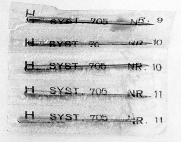 a) Symaskin av märket Husqvarna, modell V.S.4. Handdriven. Svartmålad på träplatta. Nersänkt låda med tillbehör. b) Huv av ekfaner. Handtag på toppen. c) Skyttel av stål. Rund, spetsig i ena änden, rak i den andra. Innehåller en spole med vit tråd. d) Fem spolar av stål. Rund stav med plattor i ändarna. Olika trådrester. e) Ledpressarfot (monterad på maskinen). f) Fållvikare 2 mm. g) Fållvikare 6 mm. h) Gansapparat. i) Rynkfot .j) Linjal. Längd 5,3 cm. k) Fem symaskinsnålar i olika grovlekar. Cellofanförpackning. l) Skruvnyckel. Typ lång platt nål, bakre delen försedd med runt hål. m) Skruvmejsel av stål. Fäste av svart bakelit. n) Borste av dubbelvriden ståltråd med en borste i ena änden. o) Skruvmejsel av stål. Fäste av svart bakelit. p) Provlapp av bomullsflanell. För kontroll av stygnställning. q) Provlapp av bomyllskypert. Till kontroll av stygnställning. r) Bruksanvisning. Tryckt broschyr på 30 sidor.