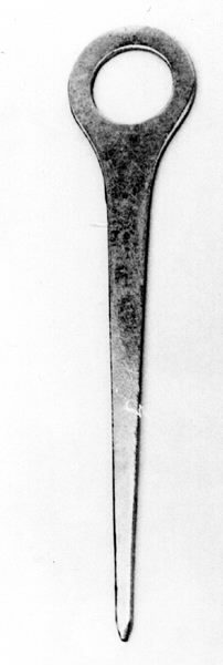 a) Symaskin av märket Husqvarna, modell V.S.4. Handdriven. Svartmålad på träplatta. Nersänkt låda med tillbehör. b) Huv av ekfaner. Handtag på toppen. c) Skyttel av stål. Rund, spetsig i ena änden, rak i den andra. Innehåller en spole med vit tråd. d) Fem spolar av stål. Rund stav med plattor i ändarna. Olika trådrester. e) Ledpressarfot (monterad på maskinen). f) Fållvikare 2 mm. g) Fållvikare 6 mm. h) Gansapparat. i) Rynkfot .j) Linjal. Längd 5,3 cm. k) Fem symaskinsnålar i olika grovlekar. Cellofanförpackning. l) Skruvnyckel. Typ lång platt nål, bakre delen försedd med runt hål. m) Skruvmejsel av stål. Fäste av svart bakelit. n) Borste av dubbelvriden ståltråd med en borste i ena änden. o) Skruvmejsel av stål. Fäste av svart bakelit. p) Provlapp av bomullsflanell. För kontroll av stygnställning. q) Provlapp av bomyllskypert. Till kontroll av stygnställning. r) Bruksanvisning. Tryckt broschyr på 30 sidor.