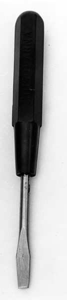 a) Symaskin av märket Husqvarna, modell V.S.4. Handdriven. Svartmålad på träplatta. Nersänkt låda med tillbehör. b) Huv av ekfaner. Handtag på toppen. c) Skyttel av stål. Rund, spetsig i ena änden, rak i den andra. Innehåller en spole med vit tråd. d) Fem spolar av stål. Rund stav med plattor i ändarna. Olika trådrester. e) Ledpressarfot (monterad på maskinen). f) Fållvikare 2 mm. g) Fållvikare 6 mm. h) Gansapparat. i) Rynkfot .j) Linjal. Längd 5,3 cm. k) Fem symaskinsnålar i olika grovlekar. Cellofanförpackning. l) Skruvnyckel. Typ lång platt nål, bakre delen försedd med runt hål. m) Skruvmejsel av stål. Fäste av svart bakelit. n) Borste av dubbelvriden ståltråd med en borste i ena änden. o) Skruvmejsel av stål. Fäste av svart bakelit. p) Provlapp av bomullsflanell. För kontroll av stygnställning. q) Provlapp av bomyllskypert. Till kontroll av stygnställning. r) Bruksanvisning. Tryckt broschyr på 30 sidor.