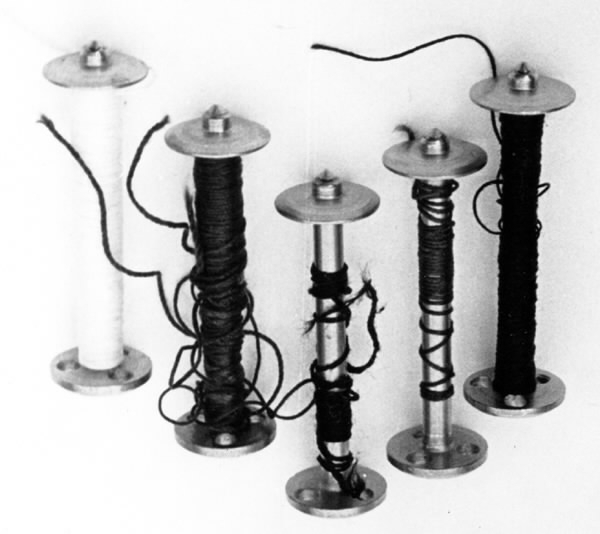 a) Symaskin av märket Husqvarna, modell V.S.4. Handdriven. Svartmålad på träplatta. Nersänkt låda med tillbehör. b) Huv av ekfaner. Handtag på toppen. c) Skyttel av stål. Rund, spetsig i ena änden, rak i den andra. Innehåller en spole med vit tråd. d) Fem spolar av stål. Rund stav med plattor i ändarna. Olika trådrester. e) Ledpressarfot (monterad på maskinen). f) Fållvikare 2 mm. g) Fållvikare 6 mm. h) Gansapparat. i) Rynkfot .j) Linjal. Längd 5,3 cm. k) Fem symaskinsnålar i olika grovlekar. Cellofanförpackning. l) Skruvnyckel. Typ lång platt nål, bakre delen försedd med runt hål. m) Skruvmejsel av stål. Fäste av svart bakelit. n) Borste av dubbelvriden ståltråd med en borste i ena änden. o) Skruvmejsel av stål. Fäste av svart bakelit. p) Provlapp av bomullsflanell. För kontroll av stygnställning. q) Provlapp av bomyllskypert. Till kontroll av stygnställning. r) Bruksanvisning. Tryckt broschyr på 30 sidor.