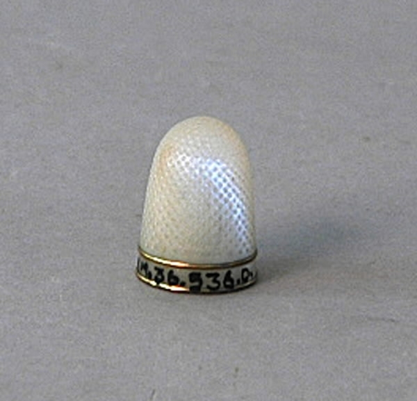 a) Syskrin av päronträ. Rektangulärt med ett metallhandtag på lockets översida och en pärlemorplatta infälld i träet under handtaget. Skrinet har fyra metallkulor som fötter. En spegel finns i lockets insida. b-c) Nåletui med lock i pärlemor med gulmetall i ett band runt etuiets lock och en stiliserad blomma, blå och grön med gul botten på etuiets framsida. d) Fingerborg av pärlemorliknande material med två gula metallringar. Höjd 2,5 cm, diameter 1,6 cm. e) Parfymflaska av slipat glas med en metallpropp. Oval tillplattad modell. Längd 5,5 cm, bredd 2,7 cm, tjocklek 0,4 cm. f) Syl av järn med pärlemorskaft. Mellan järnet och skaftet en gul metall utsmyckning. På skaftet en stiliserad blomma i blått med gul bakgrund. g) Sax av järn. Längd 5 cm, bredd 3,6 cm, tjocklek 0,2 cm. h) Sax av järn med pärlemorskaft med detaljer av gul metall. Längd 9,5 cm, bredd 3,7 cm, tjocklek 0,3 cm. i) Stoppnål av järn med dubbla ögon. Mått: längd 7 cm,  diameter 0,1 cm. j) Trådhållare av pärlemor med fyra utfällda "armar" och dekorationer i form av cirklar med mera. Längd ihopfälld 6 cm, bredd 1 cm, tjocklek 0,3 cm. 
k) Trådhållare i form av en stjärna av pärlemor med små hål i form av stjärnor. Diameter 3 cm, tjocklek 0,1 cm. l) Trådrulle i form av en stjärna av pärlemor med små hål i form av stjärnor. Mått: diameter 3 cm, tjocklek 0,1 cm. m) Trådrulle av pärlemor. Mått: längd 2,9 cm, diameter 1,5 cm. o) Insats till skrinet, trä, textil. Längd 17 cm, bredd 11,5 cm, tjocklek 0,9 cm. p) Skydd av textil som ligger mellan locket och insatsen med syutensilierna.