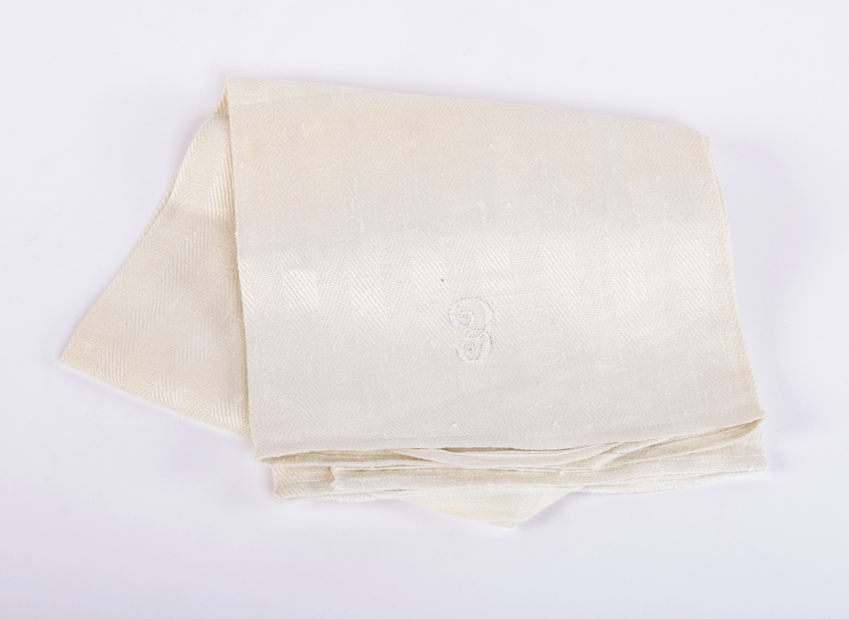 Rektangulært linhåndkle. Langsgående stipemønster i veven. Opphengs løkke på hver kortside. Brodert monogram midt på ved den ene kortsiden. Faldet på kortsiden med maskinsøm.