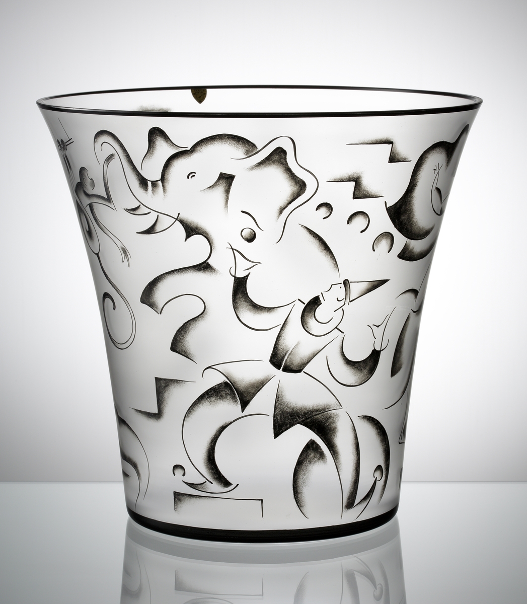 Vas "Cirkus", formgiven av Vicke Lindstrand till Stockholmsutställningen 1930. Ofärgad vas med svart mynningskant, och svartmålad dekor föreställande scener ur en cirkus: En jonglerande clown, en oklädd kvinna på en häst och en elefant.