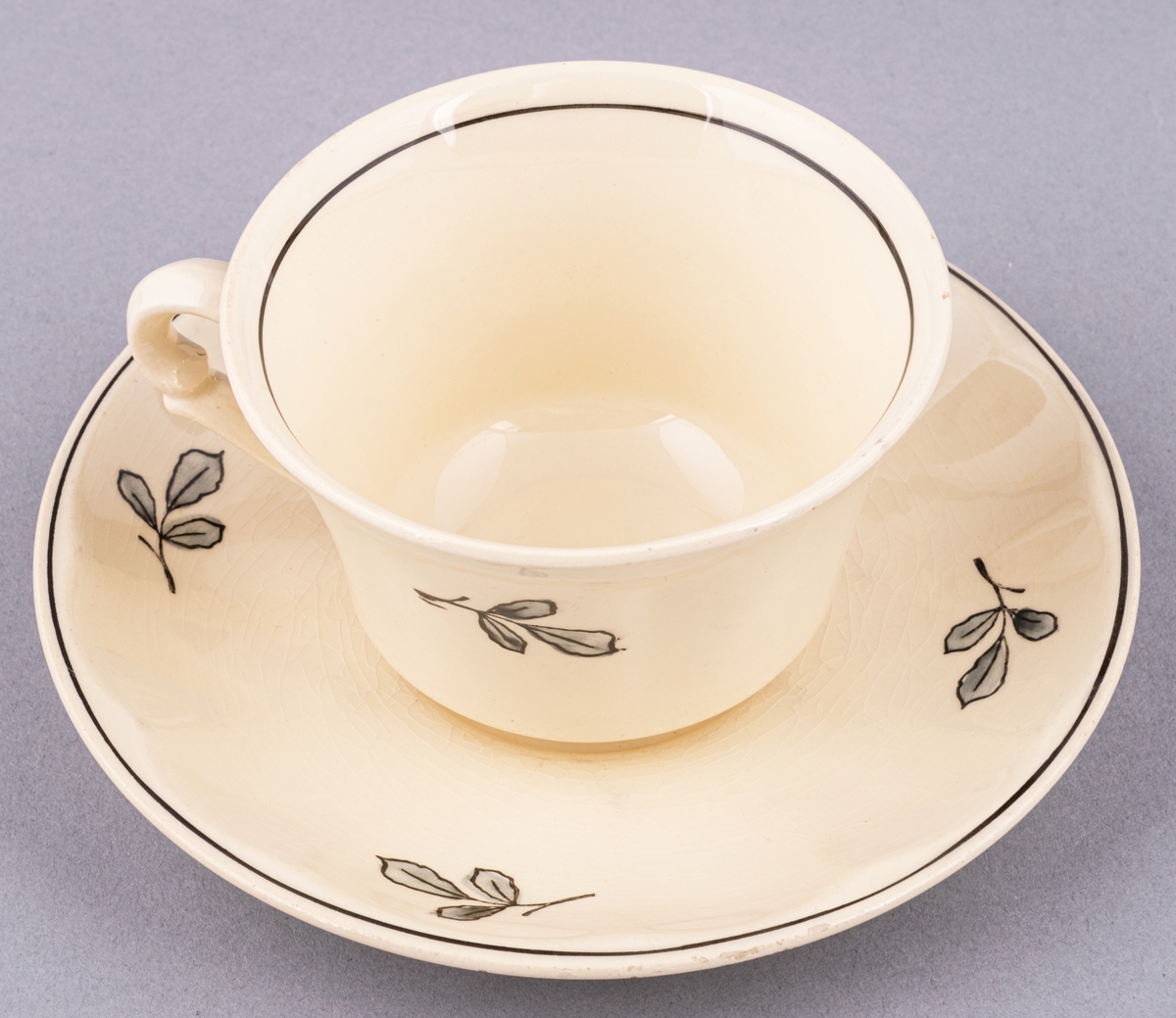 Kaffekopp med fat, i flintgods. Modell AK, dekor Bibo. Vit glasyr med flerfärgat blommönster. Skapad av Eugen Trost för Gefle Porslinsfabrik 1936.