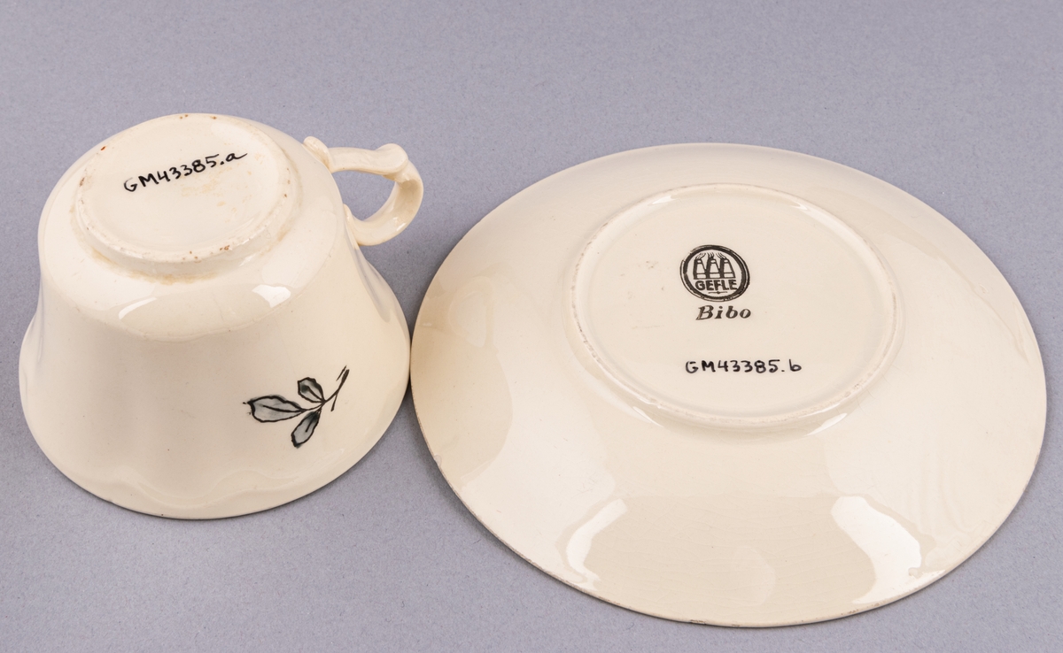 Kaffekopp med fat, i flintgods. Modell AK, dekor Bibo. Vit glasyr med flerfärgat blommönster. Skapad av Eugen Trost för Gefle Porslinsfabrik 1936.
