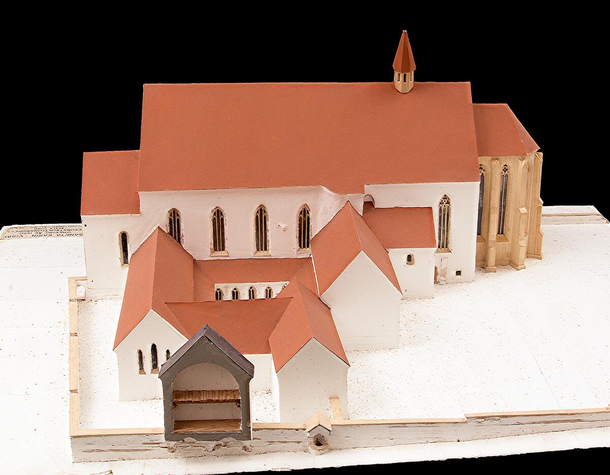 Rekonstruktionsmodell av Sankta Karin Kyrka i Visby, omkring 1450. Skala 1:100. Av trä, tak av papp. Tak målat i brunröd kulör, väggar målade i vit kulör, troligtvis med kalk- eller gipsfärg. Monterad på en spånskiva med en plakett i ena hörnet med texten: "SANKTA KARIN VISBY OMKRING ÅR 1450 REKONSTRUKTIONSMODELL SKALA 1:100 GOTLANDS FORNSAL I MAJ 1979 / [Sign Jonas Pajaujis]". Tillverkad av Jonas Pajaujis för Gotlands Museum i utställningssyfte, har varit placerad i Klosterlängan.