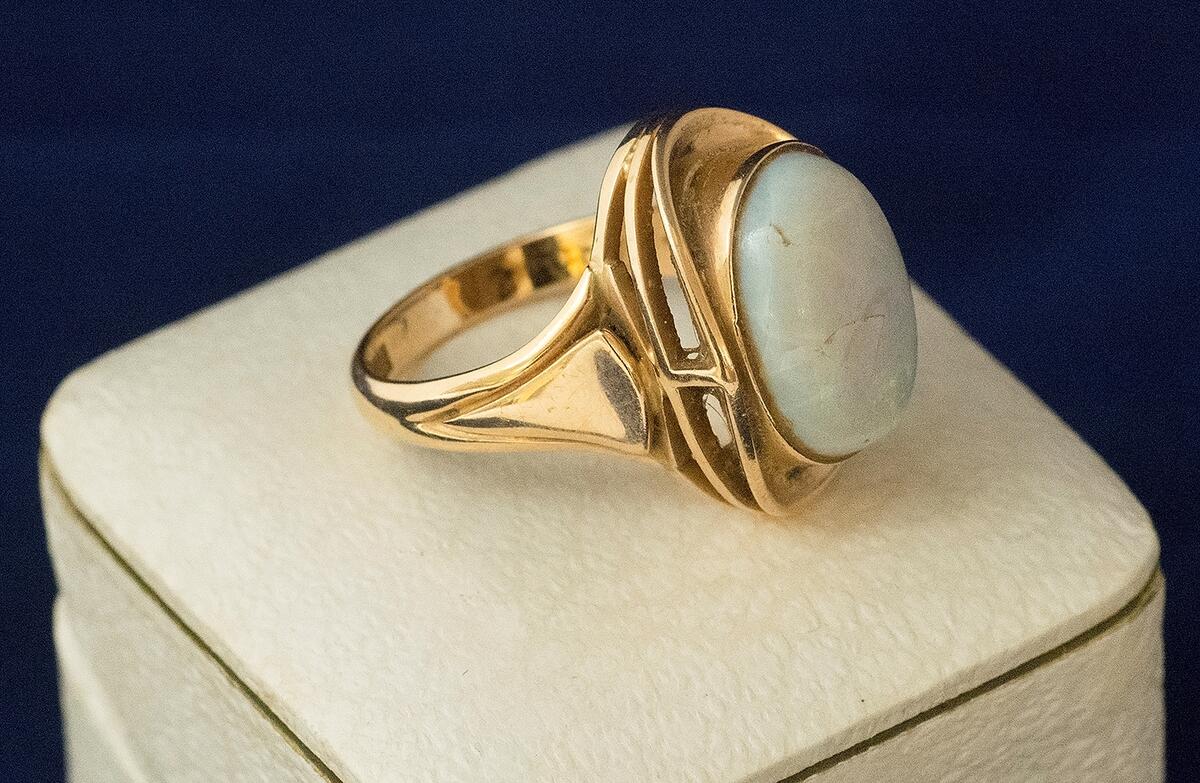 Ring, fingerring, av guld, med en oval slipad halvädelsten i ett upphöjt genombrutet fäste. Stenen gråvit med grön glans, sprucken, har lagats. Stämplar CJH (Carl Johan Häggström). Kattfot,18K, W, D10 (1978). Förvaras i ask av papp klädd i vit skinnimitation. Knäpplås. Invändigt lila sammet och trycket "C.J. Häggström Guldsmeds AB Visby".
I samlingen utan nummer