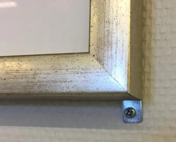 Et nærbilde som viser at et kunstverks ramme er skrudd fast i veggen.
