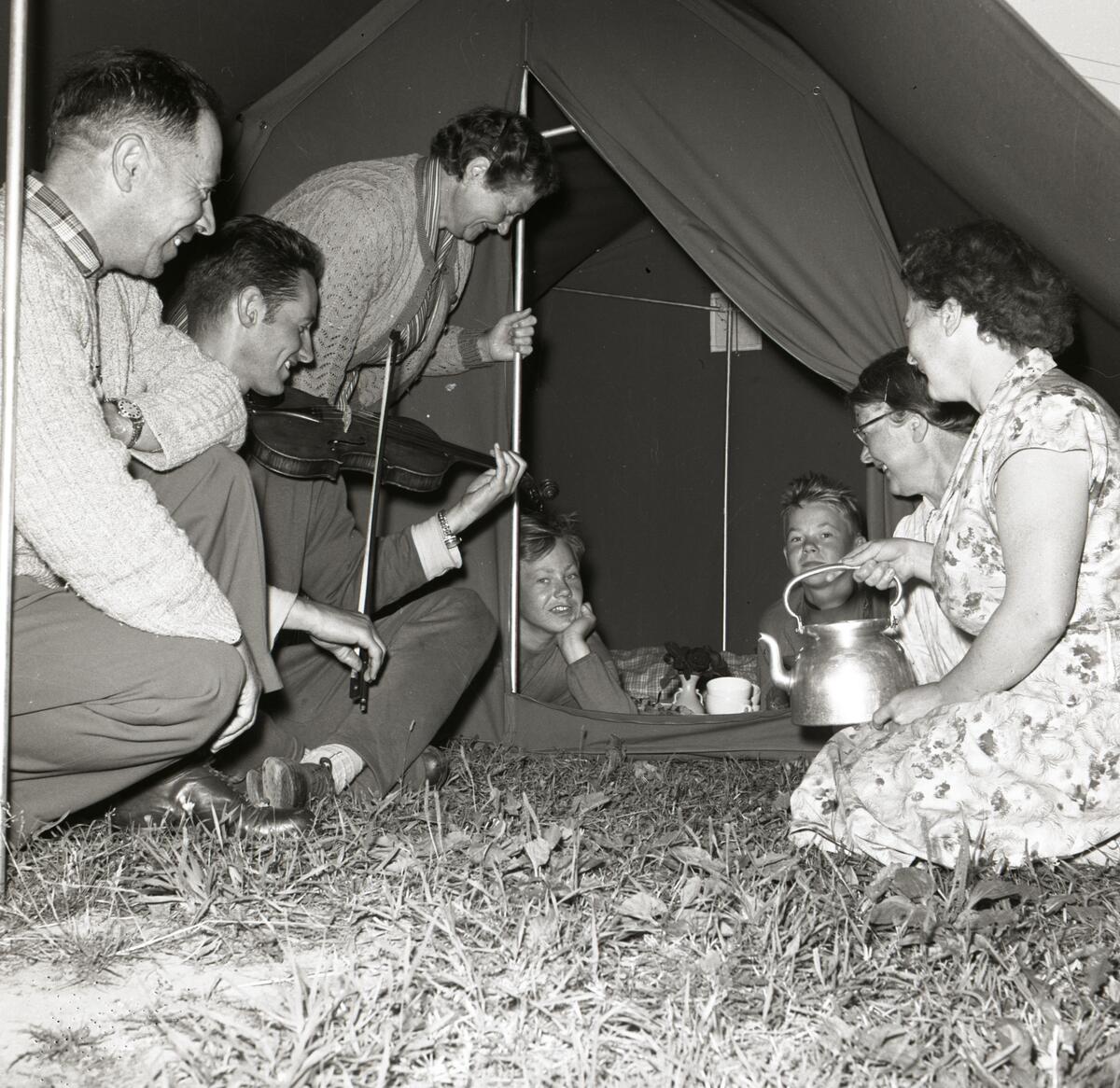 Hildings söner tittar ut genom en tältöppningen samtidigt som deras mor bjuder bekanta på fika den 29 juli 1958.