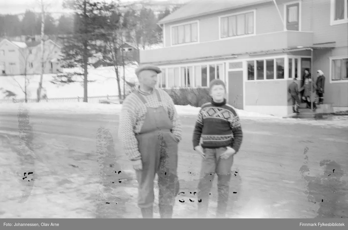 Foto av ukjent mann og gutt på gata

I bakgrunnen kan man se en kafe og en liten gruppe folk stå ved en inngangsdør 

Mannen kan være Olav Johannesen, usikker identifisering 

Foto trolig tatt på  1960/70-tallet