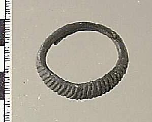 Ring av brons, öppen modell, de avsmalnande ändarna lagda omlott, "framsidan" tjockare och välvd samt ornerad med täta snedställda linjer
av brons, största tvärmått 29 mm.