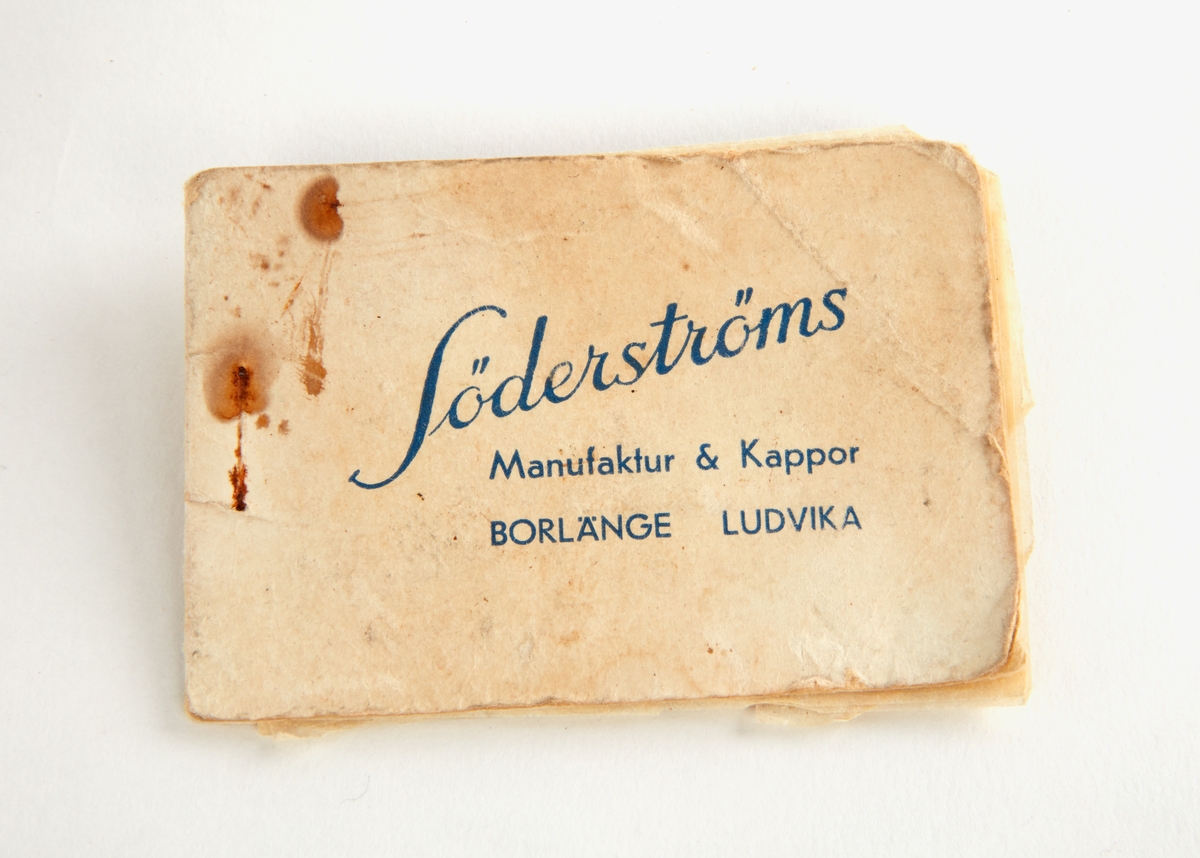 Tvål i form av tunna folieblad. Omslag av papp med text: "Tvålfolier. Söderströms manufaktur & kappor. Borlänge, Ludvika".