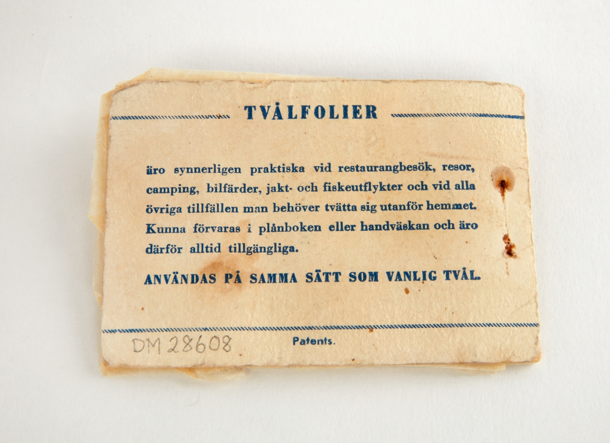Tvål i form av tunna folieblad. Omslag av papp med text: "Tvålfolier. Söderströms manufaktur & kappor. Borlänge, Ludvika".