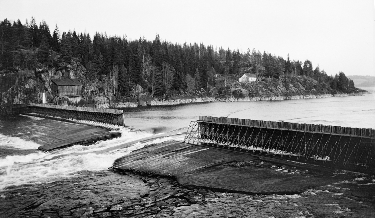 Mørkfossdammen sett fra østre mot vestre bredd.  Da fotografiet ble tatt, antakelig omkring 1920, var Mørkfoss regulert med en såkalt «fermettedam».  Dette var en konstruksjon der stengselet besto av stående plank som var reist mot ei rekke av triangulære stålbukker på tvers av vassdraget, altså en type «nåledam».  Øverst på de triangulære bukkene var det også montert gangbord der damkara kunne gå når de skulle regulere damåpningen.  Nedenfor fermettedammen er det et damgolv (flaking) - et skråplan - som overrisles av vann som har trengt mellom damplankene.  Her later detn til at damgolvet er lagt av tømmerstokker som er lagt tett i tett, parallelt med strømretningen.  Fotografiet er tatt fra den søndre elvebredden (Trøgstad-sida).  Midt i bildet ser vi en åpning i dammen - «tømmerløpet» - og på vannspeilet ovenfor aner vi hvordan fløterne hadde lagt ledelenser for å få det løstflytende fløtingtømmeret til å flyte mot denne damåpningen.  På motsatt side av elva (Spydeberg-sida) skimter vi et bergrikt landskap der det sto et skjul (til venstre) og ei lita stue (til høyre) i et terreng som ellers var dominert av barskogvegetasjon. Dammen på fotografiet ble sannsynligvis demontert vinteren 1924, for fra påfølgende vår var det den da nye dammen ved Solbergfossen som regulerte Øyeren.

Fra gammelt av var Mørkfoss en vanskelig passasje for aktørene i tømmerfløtinga.  Vassdragsingeniøren Gunnar Sætren beskrev fossen og den effekten damanlegget på stedet fikk slik (1904):

«Umiddelbart nedenfor Øieren er Mørkfossen.  Denne bestod oprindelig af tre fald, og da den var meget smal, havdes særdeles høie flomme i Øieren.  Dette forhold er nu betydelig forbedret, efterat der i aarene 1857 til 69 blev udført betydelige sprængningsarbeider til utvidelse af Mørkfossen.  Samtidig opførtes en reguleringsdam ovr Mørkfossen for at hæve lavvandet i Øieren af Hensyn til dampbaadsfarten og flødningen.  Ved disse arbeider er store flomme sænket betydelig ....»