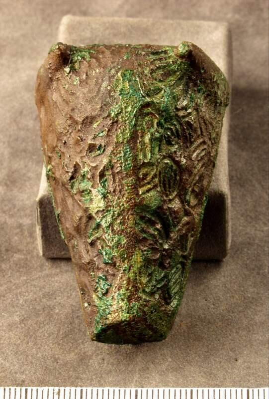 Ornamenterat i abstrakt (djur)ornamentik och ganska nött, nål saknas
djurhuvudformad, 60 x 33 mm. Utan nål, anfrätt. Funnen vid båtels i gerum.