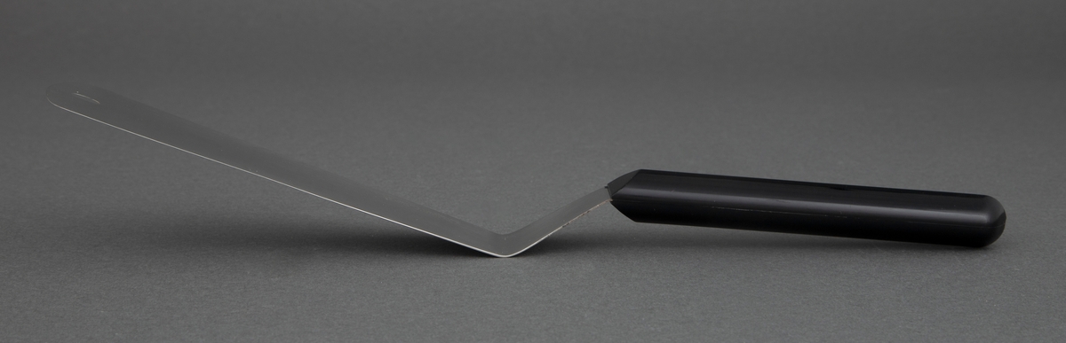 Stekespade i rustfritt stål med svart, kantete nylonskaft. Skaftet er festet rett til bladet .Utstanset oval øverst i bladet for oppheng.