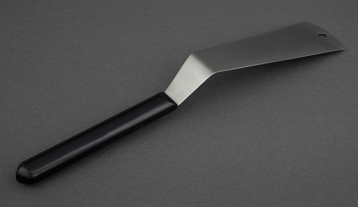 Stekespade i rustfritt stål med svart, kantete nylonskaft. Skaftet er festet rett til bladet .Utstanset oval øverst i bladet for oppheng.