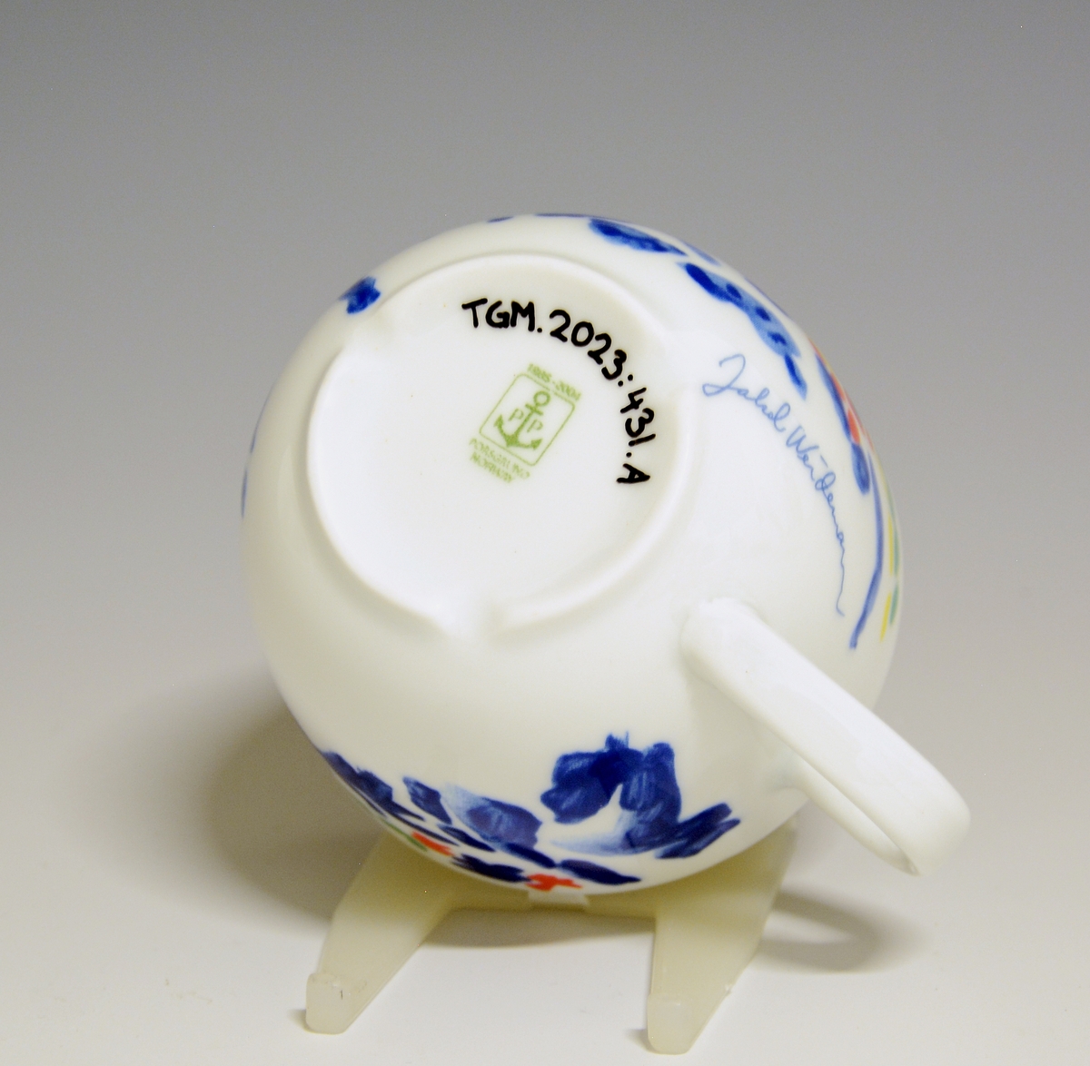 Kopp av porselen med hvit glasur. Derkorert med nonfigurativt motiv i blått, gult, grønt og rødt.
Modell: Roma av Grete Rønning
Dekor etter motiv av Jakob Weidemann